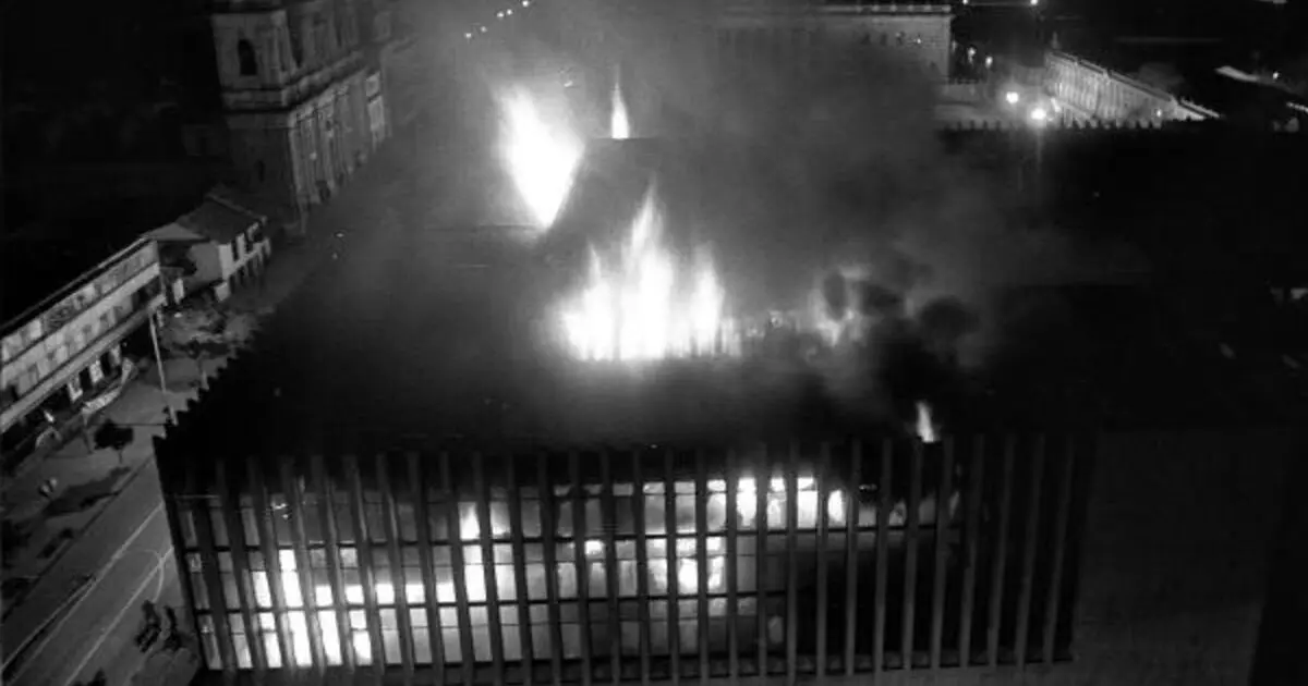 Ni perdón ni olvido para la Banda Criminal M19 2 Vista aérea nocturna del Palacio de Justicia en llamas durante el ataque del M-19, con columnas de humo elevándose sobre el centro de Bogotá, símbolo del horror y la tragedia nacional.