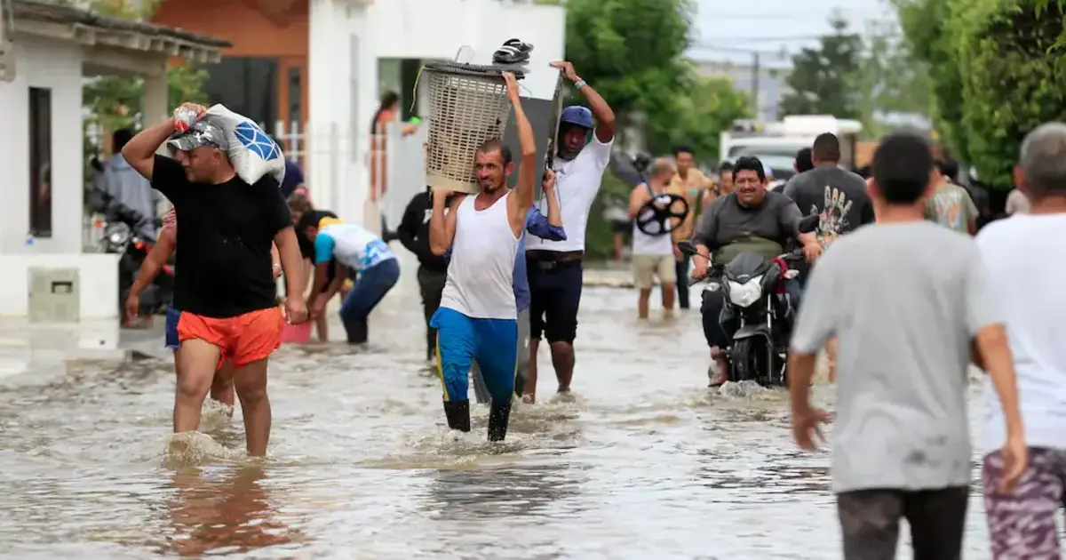 Un Mojanero más! 2 Habitantes de La Mojana caminan entre calles inundadas cargando pertenencias tras desbordamiento del río, reflejando la crisis que afecta a la población mojanera.