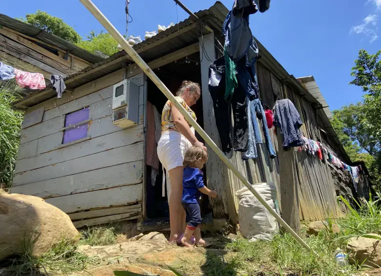 08 DE MARZO, EL PRIMER PASO 2 Madre y niño frente a vivienda precaria de madera en zona vulnerable de Colombia, imagen que refleja pobreza monetaria y condiciones de informalidad habitacional.